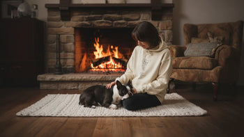 Person wearing Doggo Mojo hoodie with custom minimal line art snuggles Boston Terrier by cozy rustic stone fireplace.