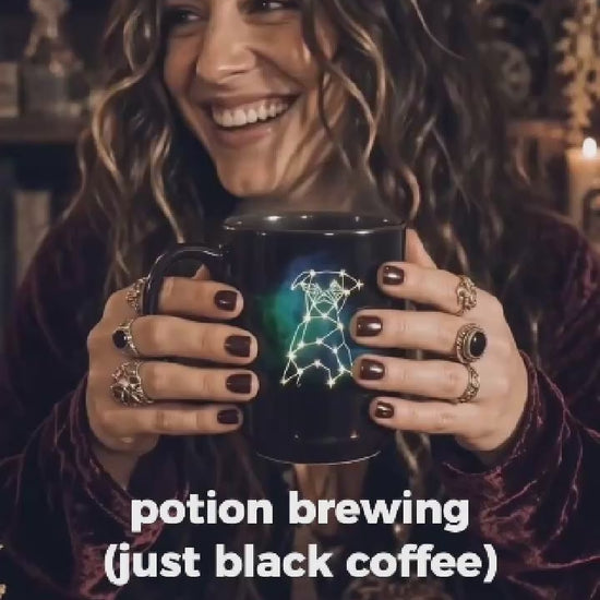 Hands holding a glossy black ceramic mug featuring a custom white line-art dog sketch and celestial stars with steam rising.